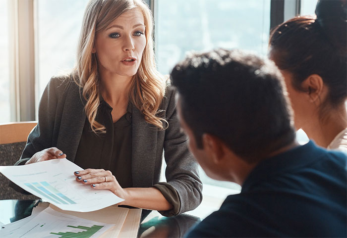 Woman speaking to clients at a desk.