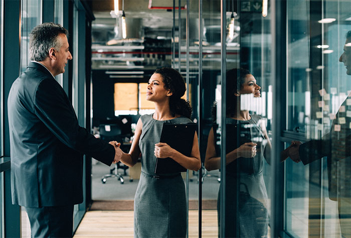 Businessman and woman shaking hands in office corridor.